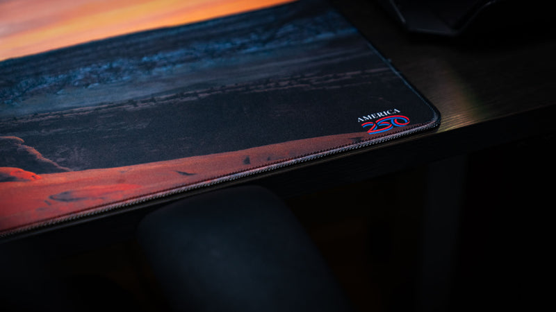 Close-up of the Delicate Arch premium deskmat featuring the America 250 emblem, precision stitched edges, and high-definition Arches National Park landscape photography.