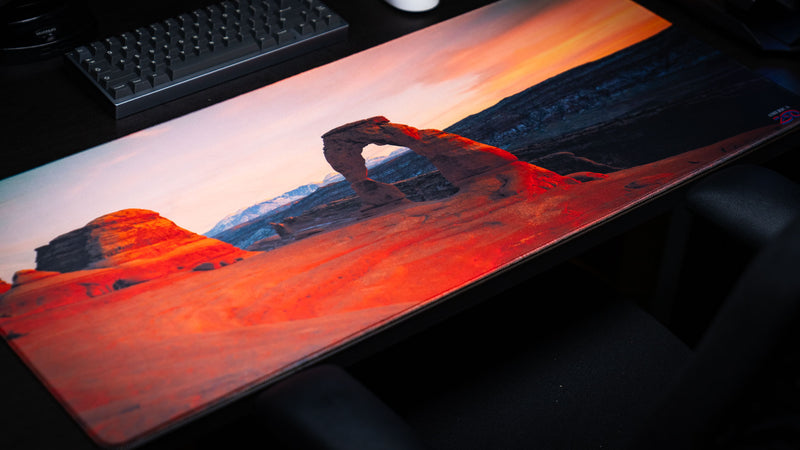 Angled view of the Delicate Arch premium deskmat featuring Arches National Park at sunrise, high-definition landscape photography, stitched edges, and a smooth gaming surface.