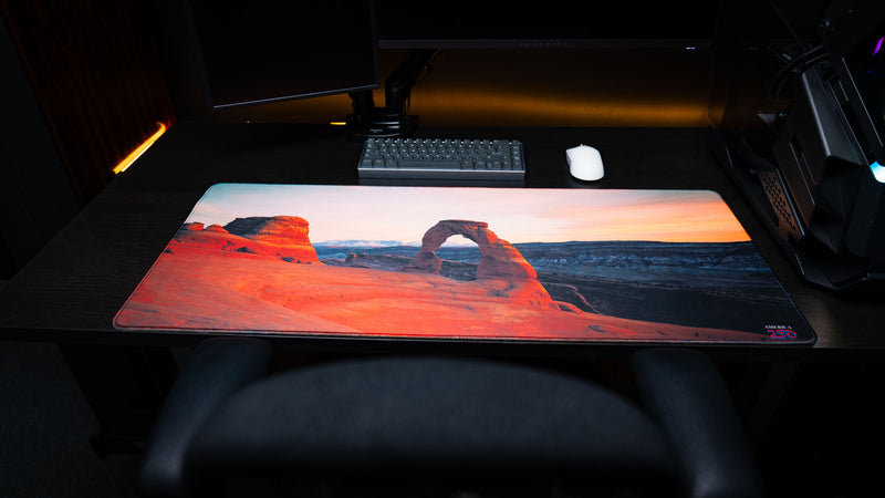 Front view of the Delicate Arch premium deskmat featuring Arches National Park at sunrise, vivid panoramic photography, stitched edges, and an extended gaming surface.