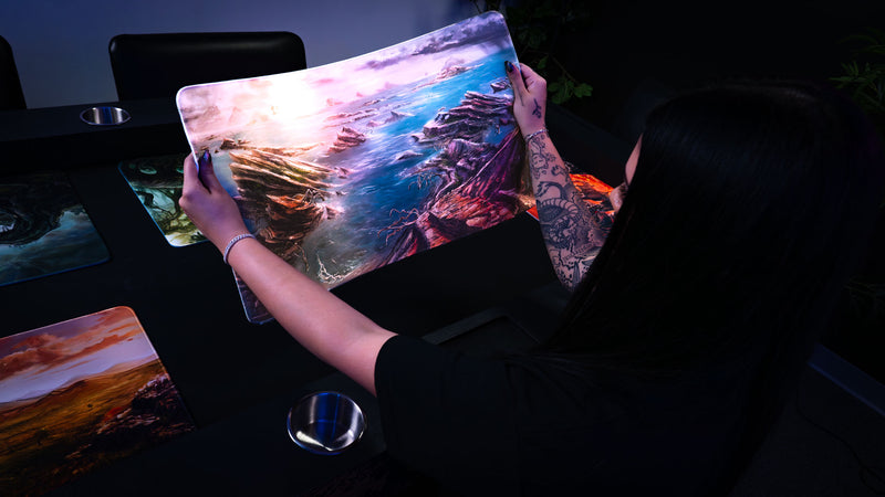 Person holding the Desolate Island fantasy playmat featuring rocky coastal cliffs, scattered islands, and blue ocean waters from the Fallen Lands collection.