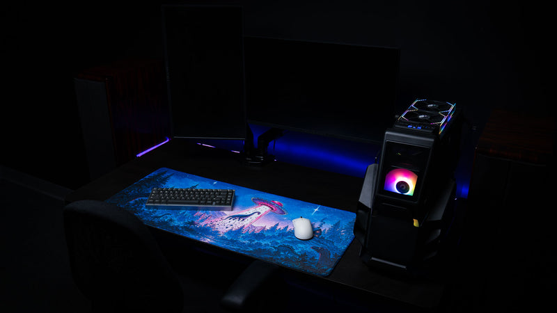 Dino Abduction Rust deskmat displayed in a gaming workstation with keyboard and mouse, featuring vibrant UFO artwork across the full desk surface.