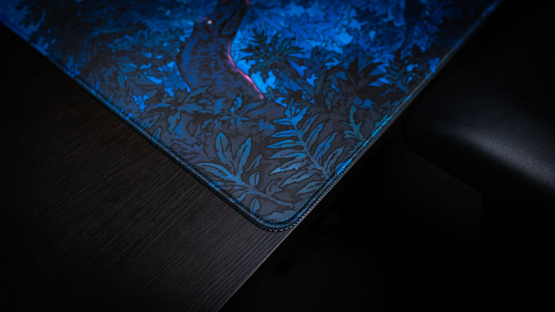 Close-up of the Dino Abduction Rust deskmat showcasing premium stitched edges, detailed forest artwork, and a smooth gaming surface.