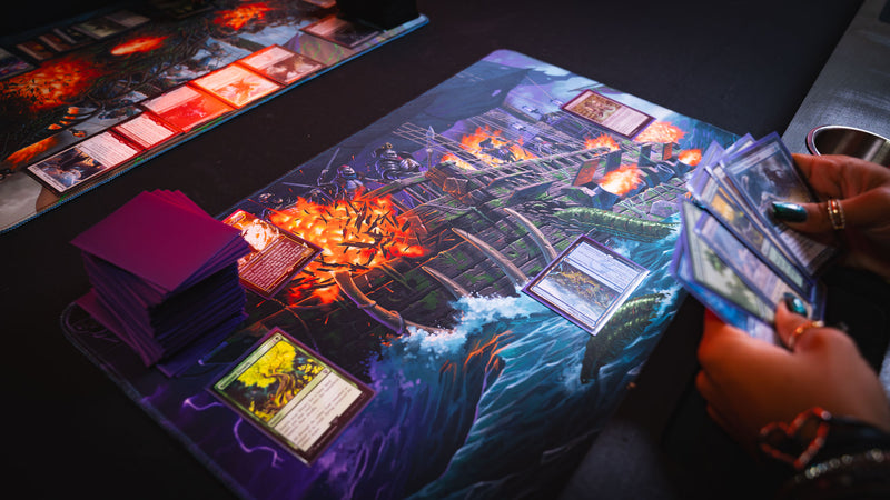 Close-up of the Dreadmarrow TCG playmat in use during a trading card game, showcasing the undead ghost ship artwork with cards, deck sleeves, and an active player.