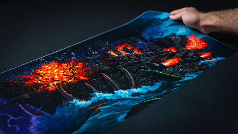 Close-up of the Dreadmarrow playmat showing its flexible cloth surface and premium construction, featuring a skeletal ghost ship battling through stormy seas with blazing cannon fire and sea monster tentacles.