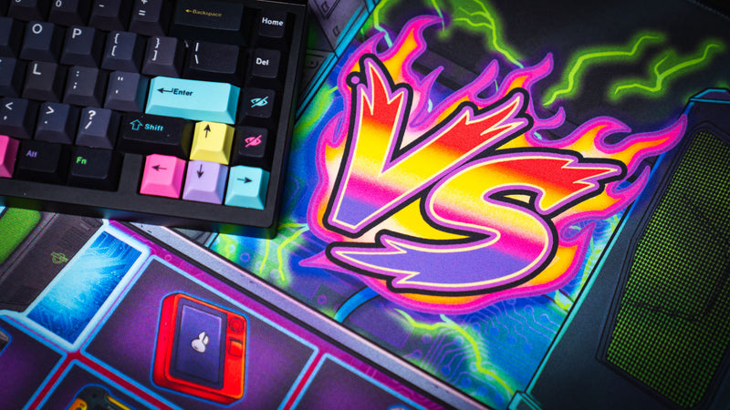 Close-up of the E-waste Showdown deskmat by Bringus Studios featuring a vibrant neon VS logo, retro gaming-inspired artwork, glowing circuitry patterns, and a colorful mechanical keyboard.