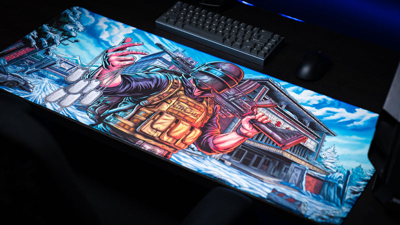 Angled view of the Extraction Boss deskmat by ImOw featuring a tactical operator with dog tags and rifle in a snowy urban setting, displayed on a premium gaming desk with vibrant colors, stitched edges, and a smooth gaming surface.