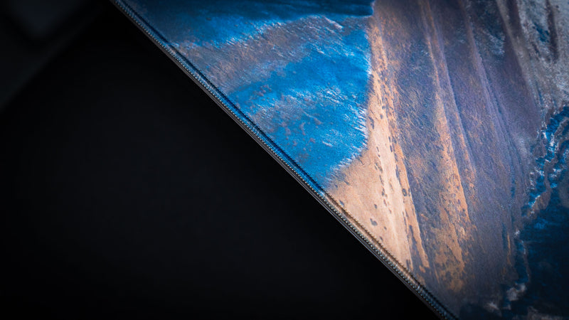 Detailed close-up of the February Snowfall deskmat highlighting premium stitched edges and vibrant mountain landscape print.