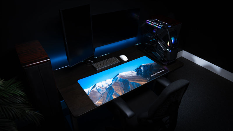 Angled desk setup showcasing the February Snowfall deskmat featuring snow-covered mountains in rural Utah beneath a vibrant blue sky from the America 250 collection.