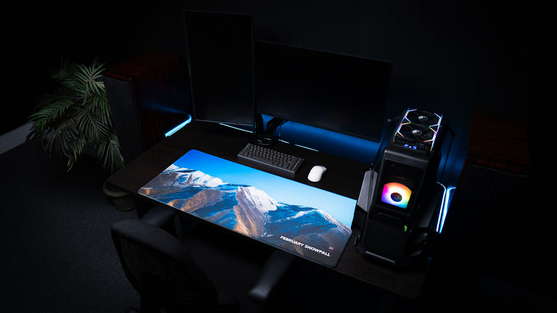 Full gaming desk setup showcasing the February Snowfall deskmat with panoramic snowy mountain landscape from rural Utah.