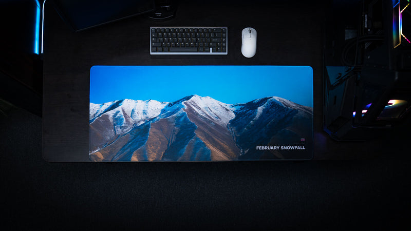 Top-down view of the February Snowfall panoramic deskmat displaying snow-covered Utah mountains across a full-size desktop.