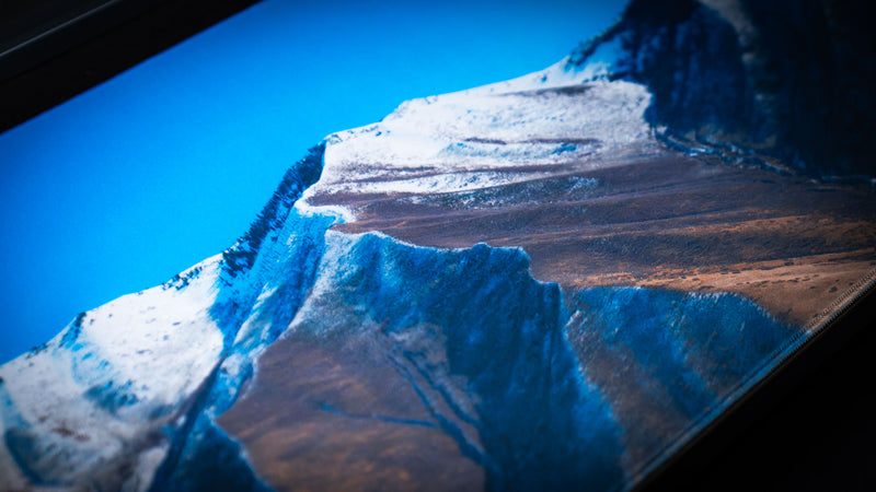 Macro view of the February Snowfall deskmat showing crisp print quality of snow-covered Utah mountain ridges and blue sky.