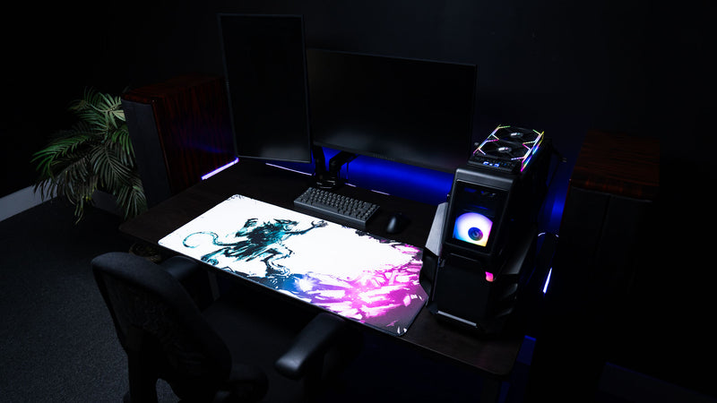 Angled view of the Forbidden Spoils premium XXL gaming deskmat in a modern desktop setup, showcasing the fantasy rat warrior artwork with purple crystal accents, keyboard, mouse, and RGB gaming PC.