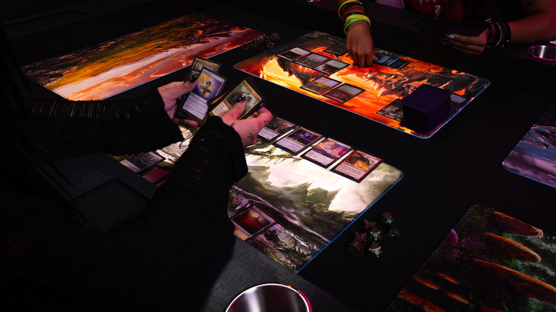Player using the Forsaken Swamp fantasy playmat during a tabletop card game, featuring a misty swamp landscape with twisted trees and rocky terrain.