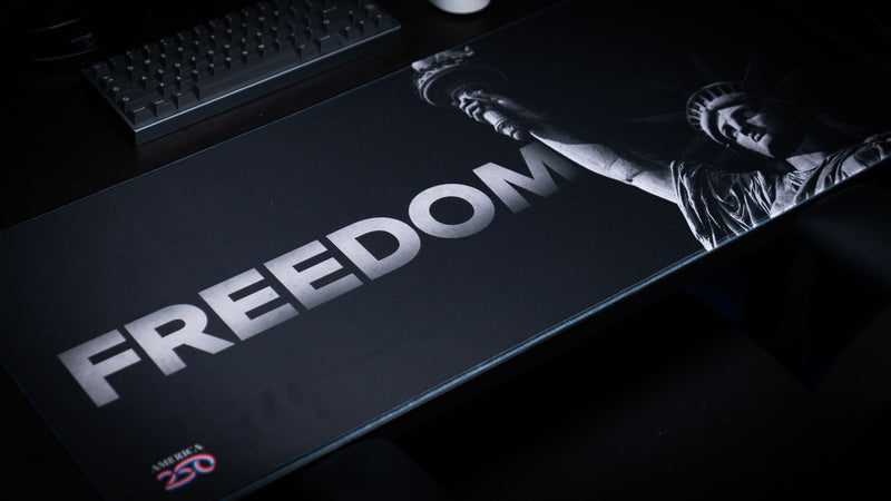 Angled view of the Freedom deskmat featuring a monochrome Statue of Liberty with bold "FREEDOM" typography, stitched edges, premium extended gaming mouse pad, and minimalist patriotic design.