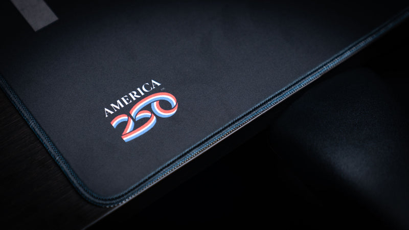 Close-up of the Freedom deskmat corner featuring the America 250 logo, premium stitched edges, smooth cloth surface, and durable extended gaming mouse pad construction.