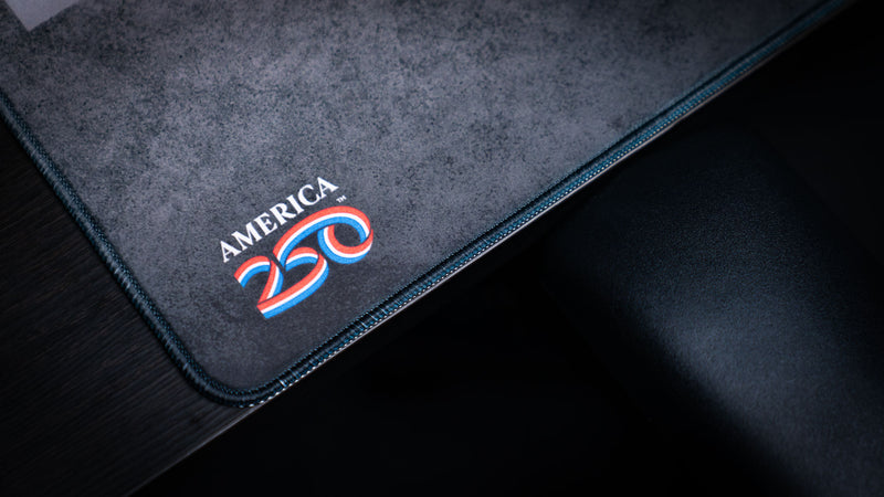 Close-up of the Freedom deskmat featuring the America 250 commemorative logo, textured gray surface, premium stitched edge, and durable gaming desk mat construction.