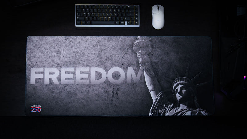 Top-down view of the Freedom deskmat featuring a distressed black-and-gray Statue of Liberty design with bold "FREEDOM" typography and the America 250 logo.