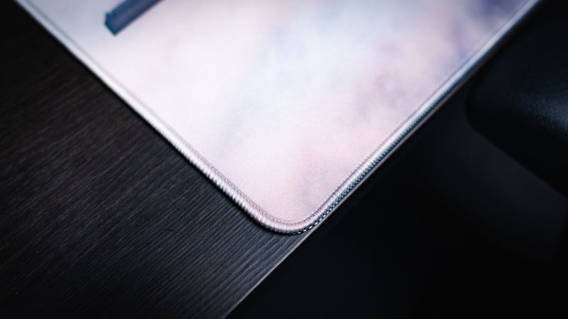 Close-up of the Freedom in the Sky deskmat corner showing soft cloud artwork, light fabric texture, and stitched edge detail.