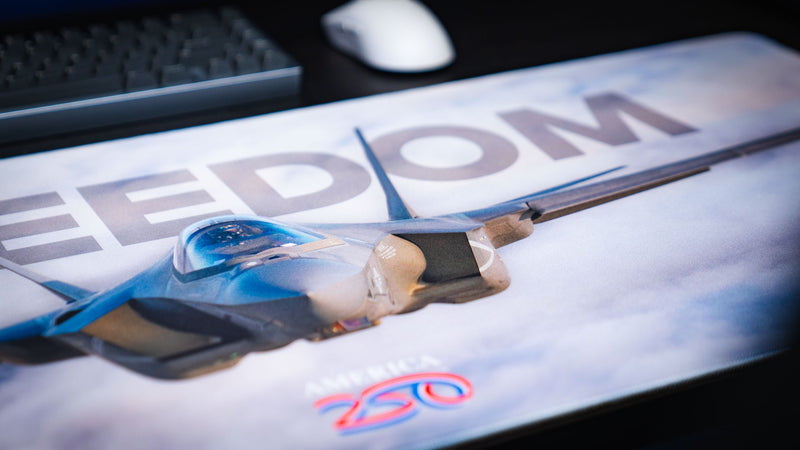 Close-up of the Freedom in the Sky America 250 deskmat showing the fighter jet cockpit, cloudy sky print, and bold FREEDOM lettering.
