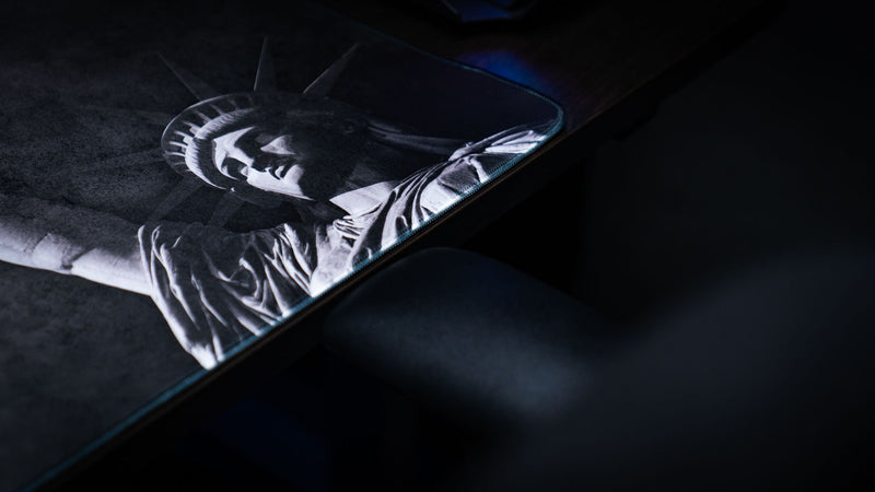 Detailed close-up of the Freedom deskmat featuring the Statue of Liberty artwork, textured grayscale finish, and premium stitched edge on an oversized gaming desk mat.