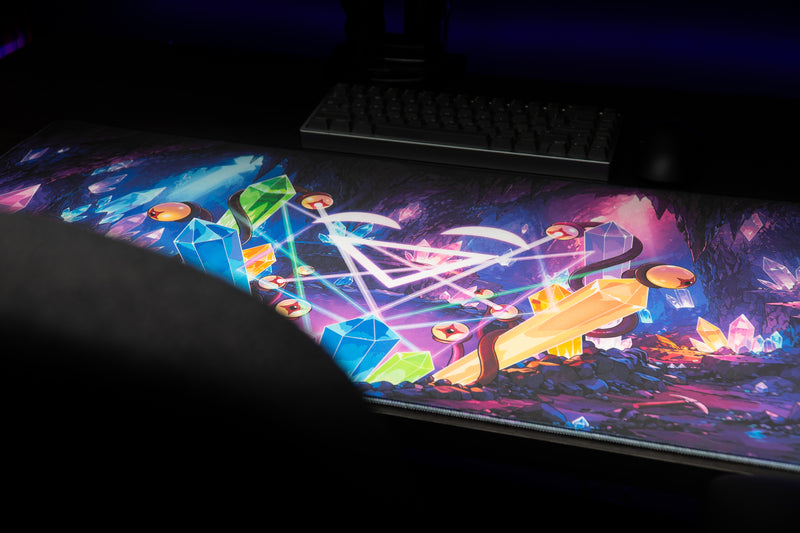 GHOSTYMPA's Perplexray's Paradise deskmat partially rolled on a desk, showing blue, pink and orange crystal artwork.