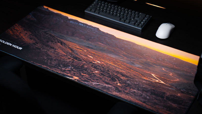 Angled view of the Golden Hour deskmat featuring winding desert roads, orange sunset light, Arches National Park scenery, keyboard, and white mouse.