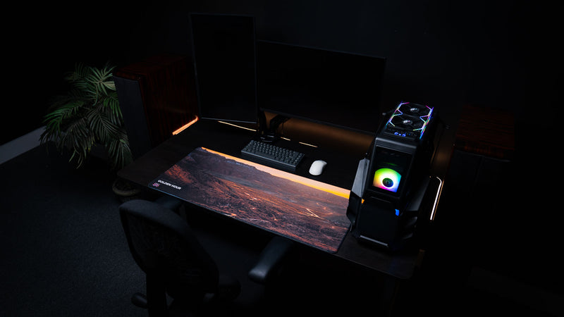 Golden Hour America 250 deskmat displayed in an RGB PC setup with sunset desert artwork, keyboard, mouse, and warm accent lighting.