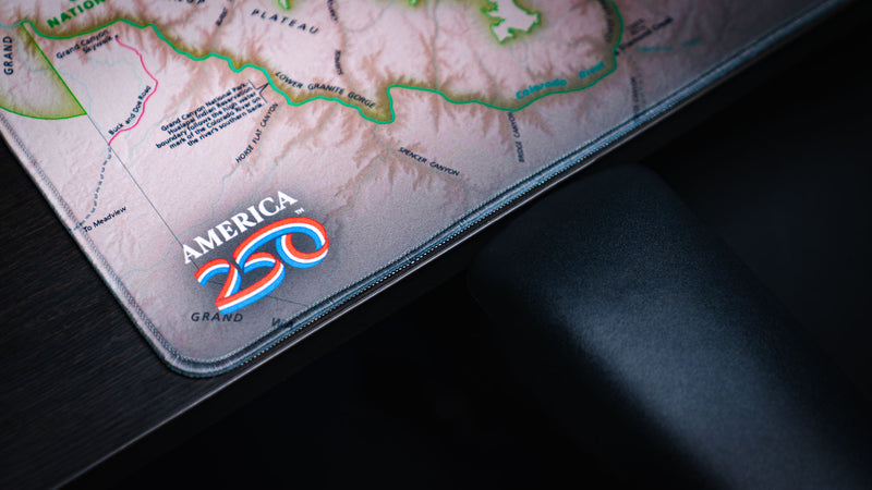 Close-up of the Grand Canyon Green deskmat showing stitched edges, detailed topographic map artwork, and the America 250 commemorative logo in the corner.