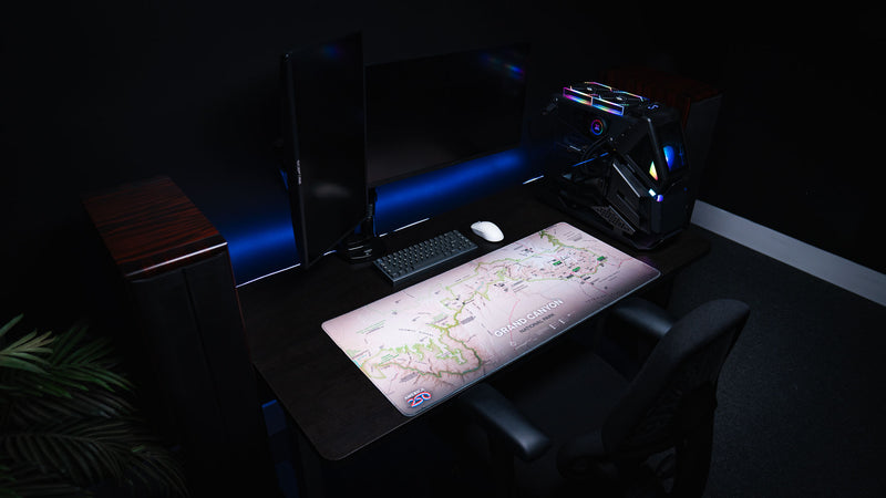 Grand Canyon Green topographic map deskmat displayed on a modern gaming desk setup with dual monitors, stitched edges, and detailed Grand Canyon National Park artwork.