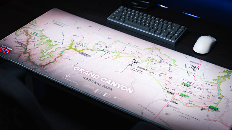 Angled view of the Grand Canyon Green deskmat featuring a detailed Grand Canyon National Park topographic map on a modern gaming desk with a mechanical keyboard and mouse.