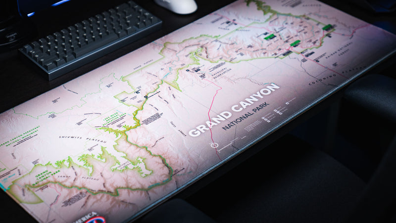 Angled close-up of the Grand Canyon Green deskmat featuring a detailed topographic map of Grand Canyon National Park with stitched edges on a gaming desk.