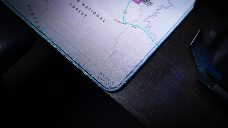 Close-up of the Grand Canyon Purple deskmat highlighting the premium stitched corner, textured topographic map artwork, and durable edge construction.