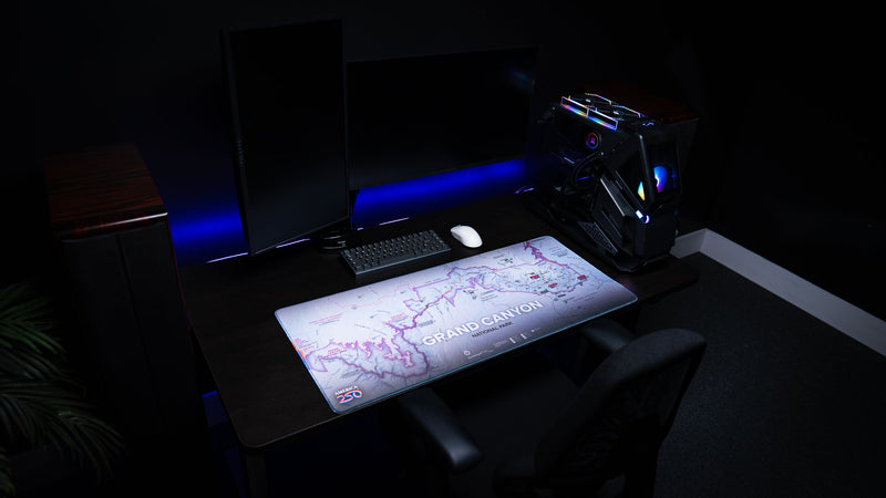 Grand Canyon Purple deskmat featuring a purple-themed topographic map of Grand Canyon National Park displayed on a modern RGB gaming desk with dual monitors and a custom PC.