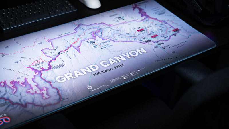 Angled close-up of the Grand Canyon Purple deskmat featuring a detailed purple topographic map of Grand Canyon National Park on a modern gaming desk.