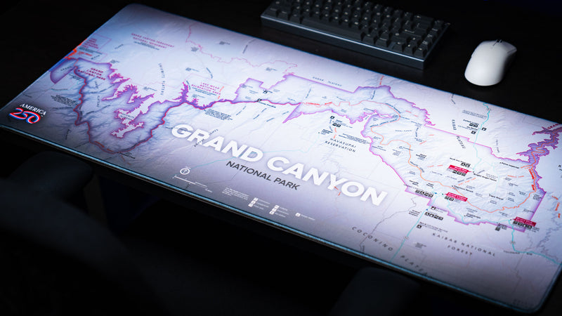Perspective view of the Grand Canyon Purple deskmat showcasing a detailed purple topographic map of Grand Canyon National Park on a modern gaming desk with a mechanical keyboard and mouse.
