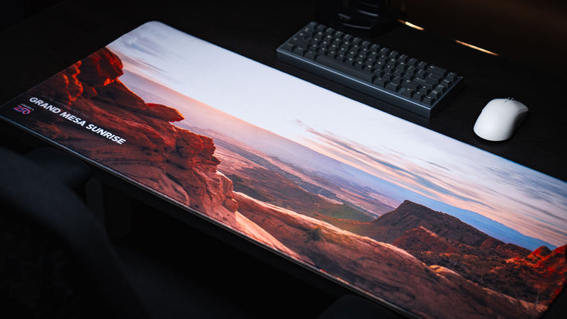 Angled view of the Grand Mesa Sunrise America 250 deskmat featuring Canyonlands sunrise scenery, red rock cliffs, keyboard, and white mouse.