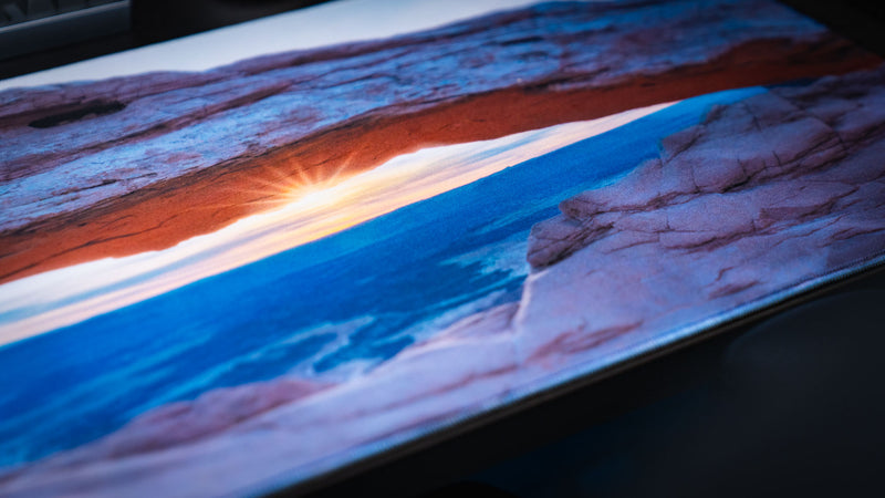 Close-up of the Grand Mesa Sunrise deskmat highlighting Mesa Arch glowing at sunrise in Canyonlands National Park with vivid HD detail, smooth fabric, and premium stitched edges.