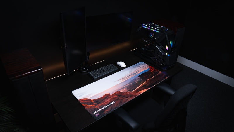 Grand Mesa Sunrise America 250 deskmat displayed in a dark RGB workspace with Canyonlands sunrise artwork, red rock cliffs, keyboard, mouse, and PC.