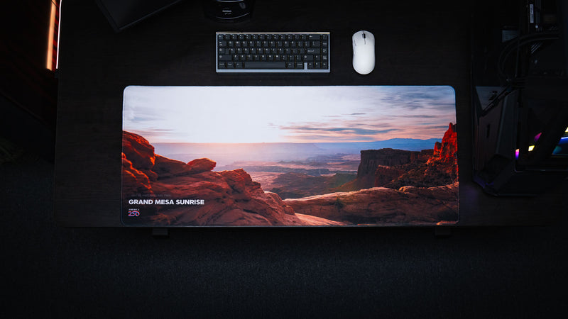op-down view of the Grand Mesa Sunrise America 250 deskmat featuring Canyonlands sunrise scenery, red rock cliffs, keyboard, and white mouse.