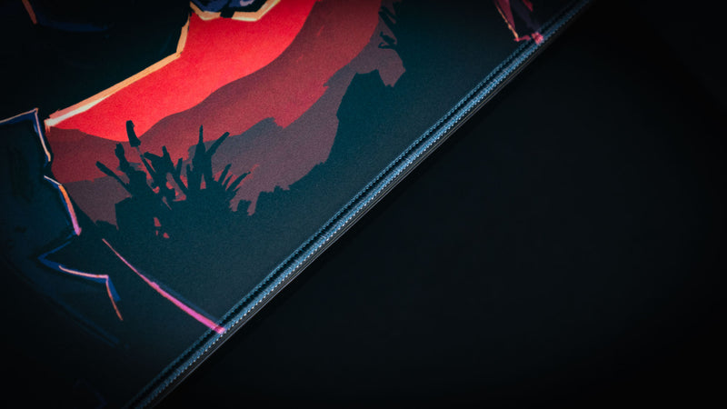 Close view of the stitched edge and red landscape artwork on the Redemption on the Old Road desk mat