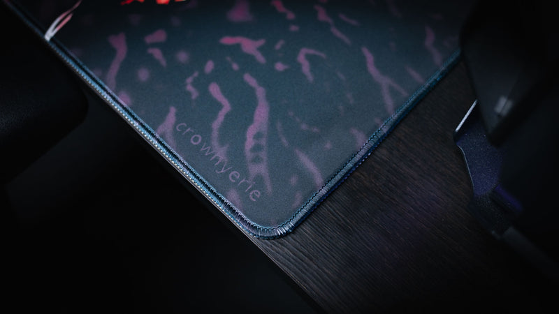 Close view of the stitched corner and creator signature on the Grim Kleeper Spare Them desk mat