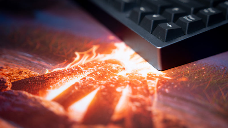 Close-up of the orange campfire artwork and fabric surface on Hens The Last Campfire deskmat beneath a keyboard.