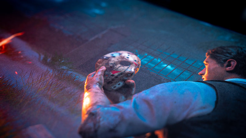 Close-up of a man holding a weathered hockey mask in the artwork on Hens The Last Campfire deskmat.
