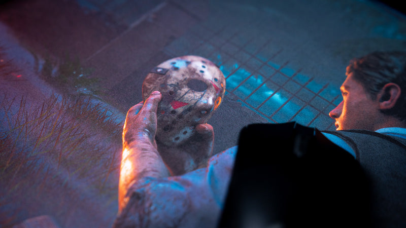 Black gaming mouse on Hens The Last Campfire deskmat beside the hockey mask and seated character artwork.