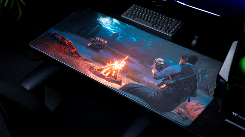 Angled view from the right of Hens The Last Campfire deskmat on a dark gaming desk beside a keyboard.