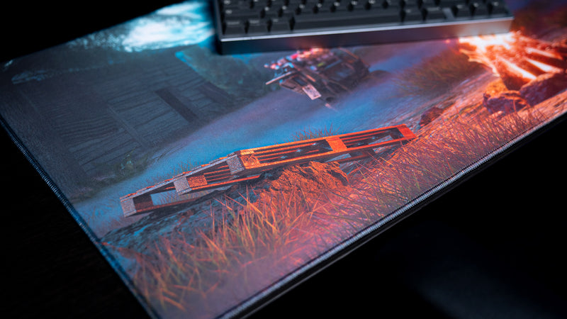 Wooden pallet and abandoned shack artwork on Hens The Last Campfire deskmat, with the stitched edge visible.