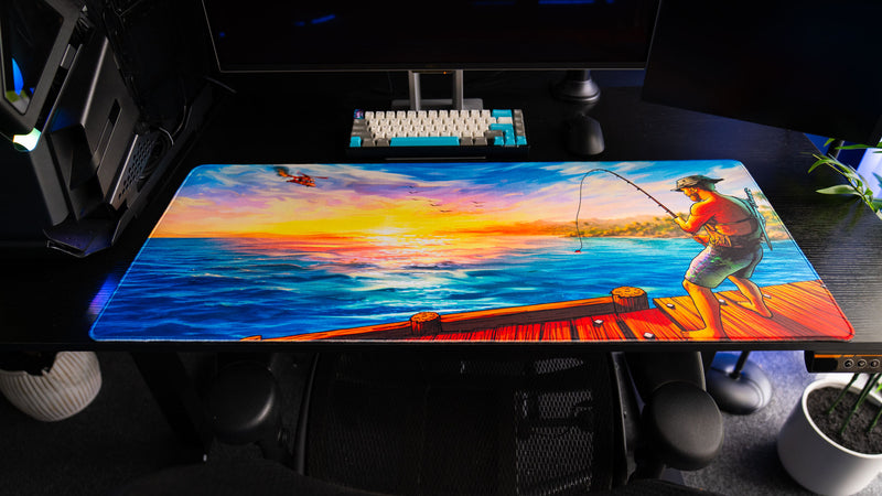 Full view of Posty's How Do You Fish deskmat featuring a fisherman on a dock, vibrant ocean waters, colorful sunset skies, and a helicopter in the distance.