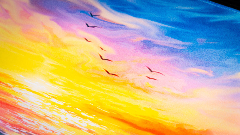 Close-up detail of Posty's How Do You Fish deskmat highlighting colorful sunset clouds, ocean reflections, and birds flying overhead.