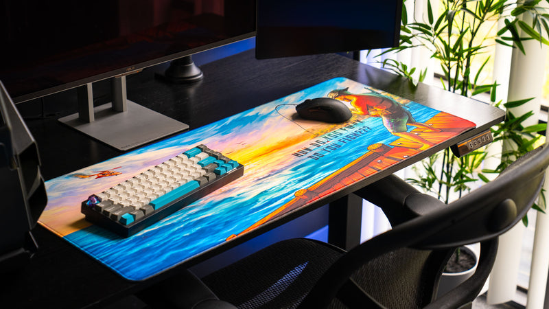 Angled desk setup featuring the How Do You F@#K Do You Fish deskmat by Posty with vibrant sunset ocean artwork, mechanical keyboard, gaming mouse, and premium stitched edges.