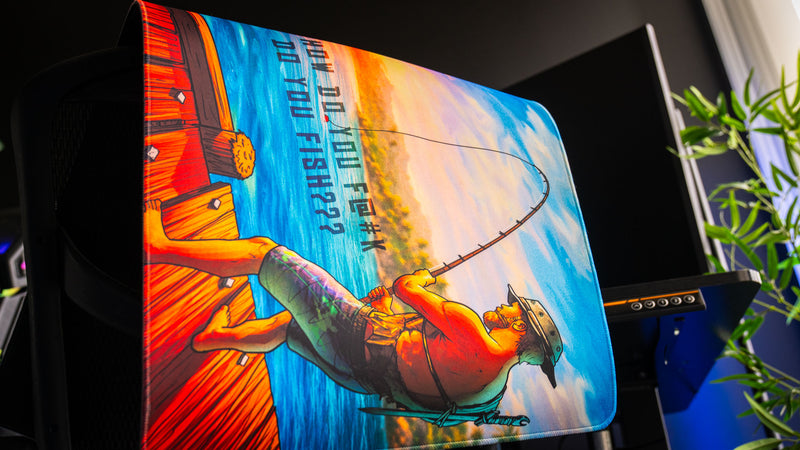 Side profile view of the How Do You F@#K Do You Fish deskmat by Posty, showing vibrant sunset artwork, fisherman illustration, stitched edges, and premium thickness.